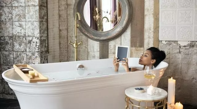 Beautiful woman reads a book in a bathtub after spray tan