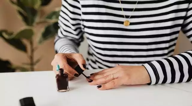 a woman with black and white top applying black nail polish