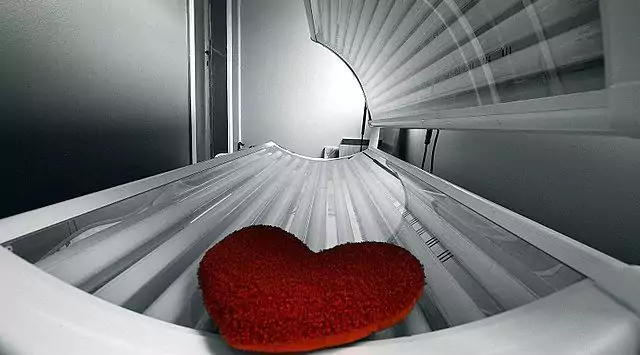 This is a black and white image of a tanning bed with a red love pillow on it